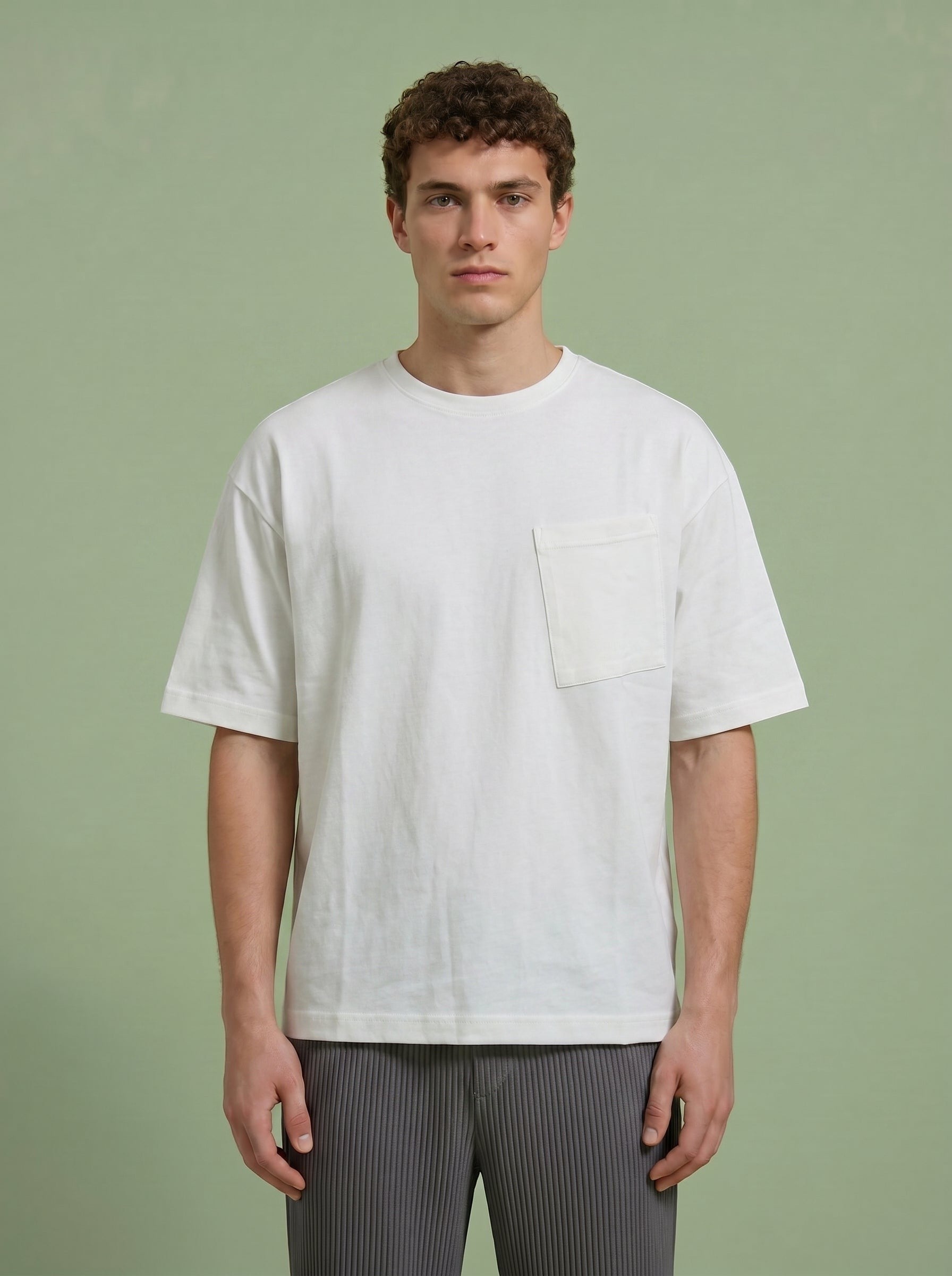 Hilos Apparel white oversized cotton blend t-shirt with crewneck and chest pocket. Model is wearing grey pleated pants.