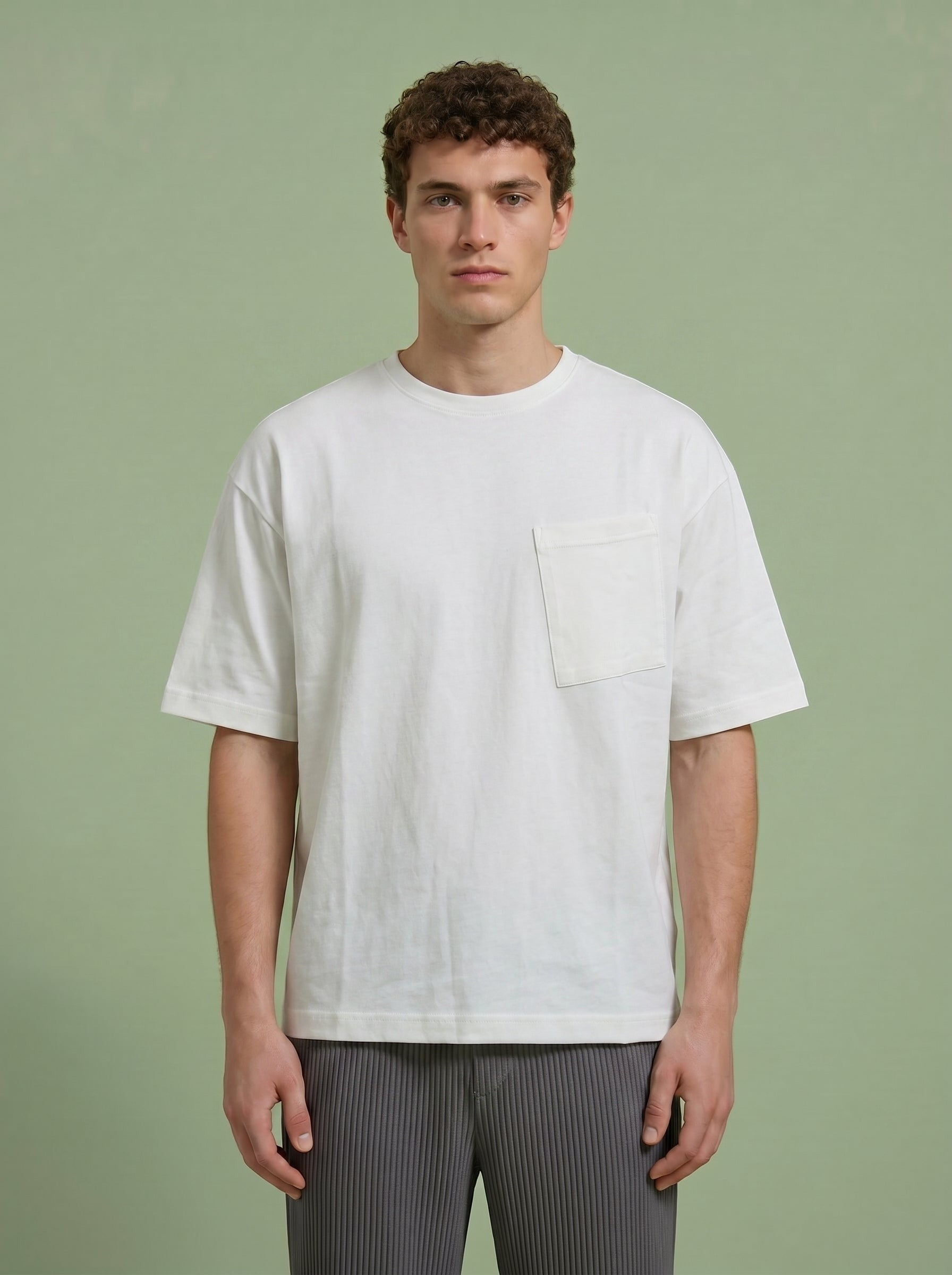 Hilos Apparel white oversized cotton blend t-shirt with crewneck and chest pocket. Model is wearing grey pleated pants.